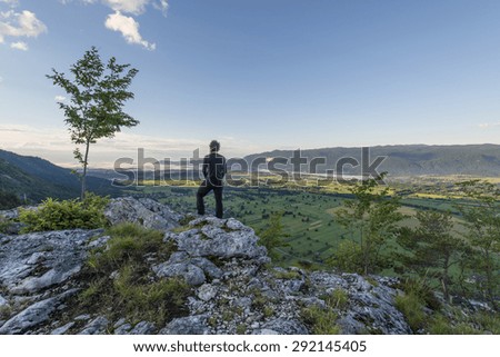 Man standing at the top of the hill and taking photos of the picturesque valley below. Vivid colors of the meadows and fields.