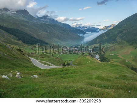 Road to Furka mountain pass in Switzerland just after the storm. Foggy and cloudy conditions with epic view in the back.