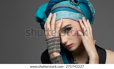 Romantic portrait of young woman in a turquoise turban with jewelry on a gray background