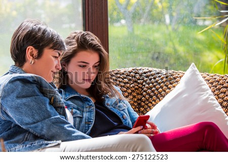 Mother and daughter sitting in a couch looking at the daughters smartphone.