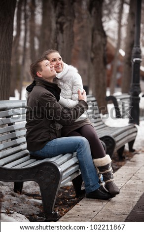Young couple sitting on bench in winter park and looking up