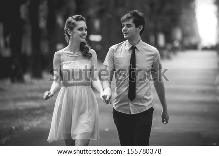 Black and white photo of young couple walking in park and holding hands