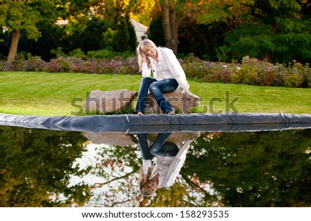 Fashionable woman sitting on rock under tree near big lake