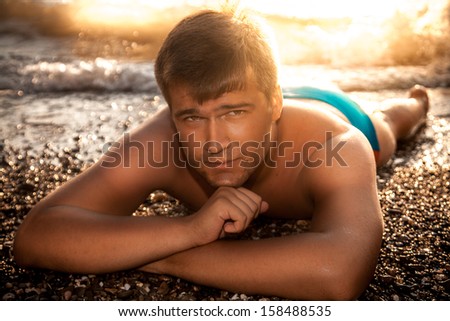 Handsome tanned man in blue swimming trunks lying on sea shore