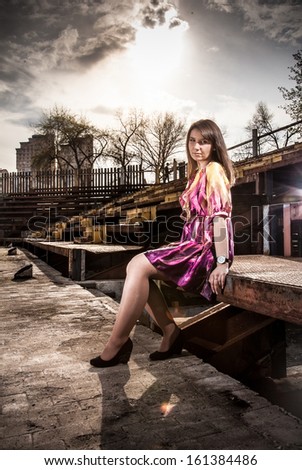 Young beautiful woman in dress sitting on bench in old rusty building
