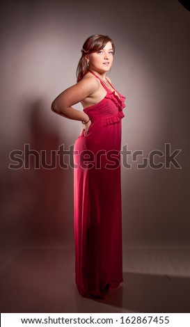Sexy brunette woman in red cocktail dress posing in studio at spot light
