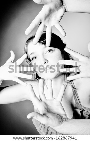 Black and white portrait of brunette girl surrounded by four hands