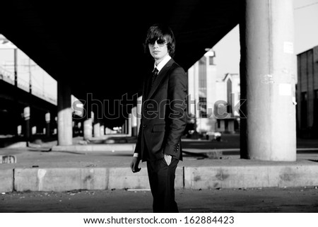Black and white portrait of man in suit wearing glasses against grunge city landscape