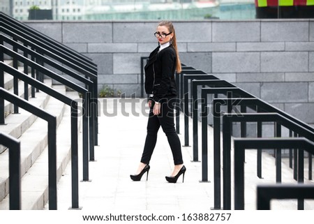 Sexy woman in black suit walking on stairs with railings at street