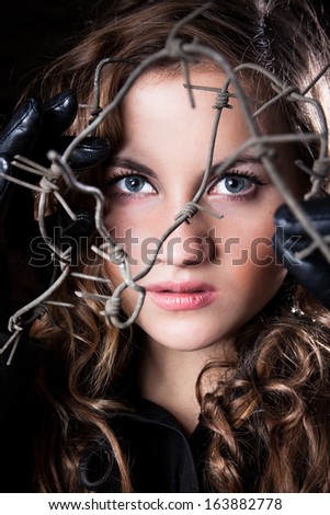 Closeup portrait of curly woman with blue eyes posing behind barbed wire