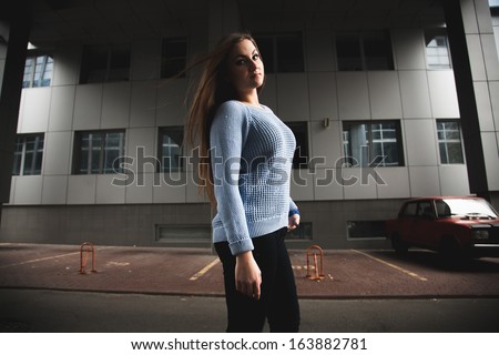 Sexy blond woman in blue sweater walking on street and looking over shoulder
