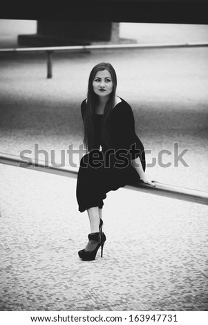 Black and white photo of sexy woman in black dress sitting on pipe in empty pool