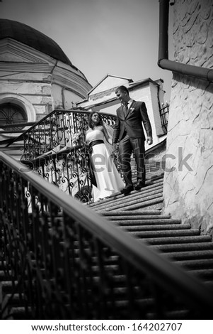 Black and white photo of bride and groom holding hands and descending from stairway