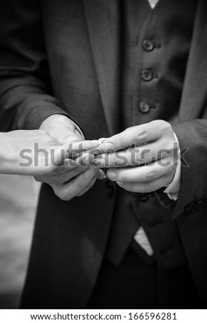 Black and white closeup photo of groom putting ring on brides hand