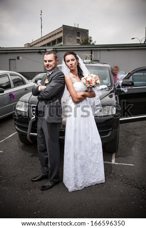 Young bride and groom standing back to back on car parking