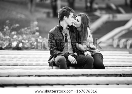 Monochrome photo of young couple in love kissing on bench