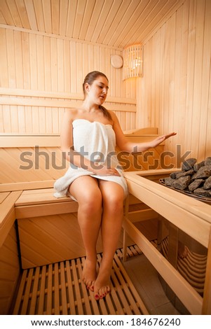 Beautiful woman holding hand over oven at sauna