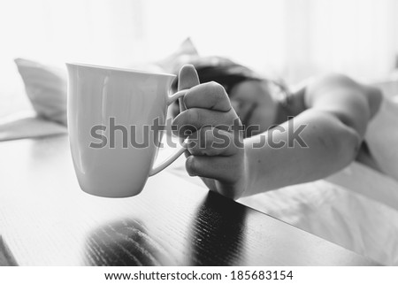 Black and white portrait of woman in bed taking cup from table
