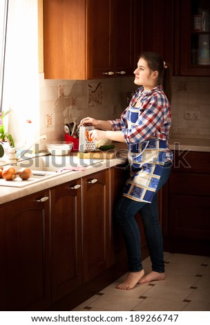 Young housewife working on classic wooden kitchen with big window