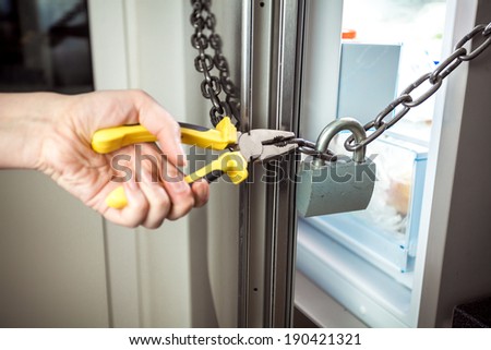 Closeup photo of woman cutting chain on fridge with pliers