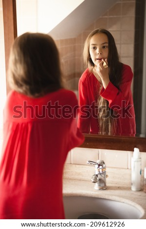 Closeup portrait of little girl painting lips with red lipstick
