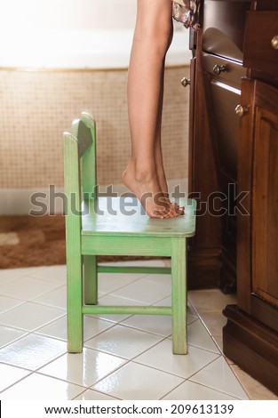 Closeup photo of little girl standing on tiptoes on chair at bathroom
