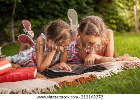 Cute girls lying on grass at park and looking at old family photos