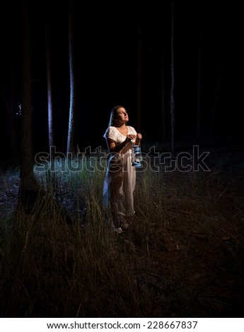 Lonely woman with gas lamp  standing in scary dark forest