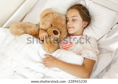 Little cute girl sleeping and hugging big teddy bear at bed