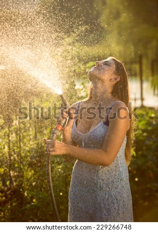 Beautiful young woman watering garden with hose pipe