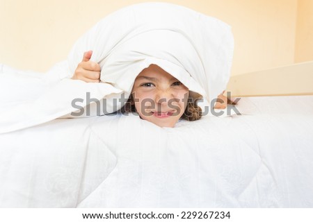 Closeup portrait of little angry girl lying in bed with pillow on head