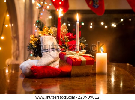 Christmas candles, gift box and woolen sock placed on table against fireplace