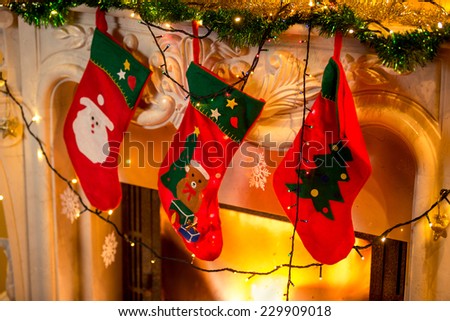 Closeup photo of three red christmas socks hanging on burning fireplace