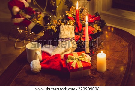 Toned photo of christmas candles, open gift box and woolen socks on wooden table at fireplace