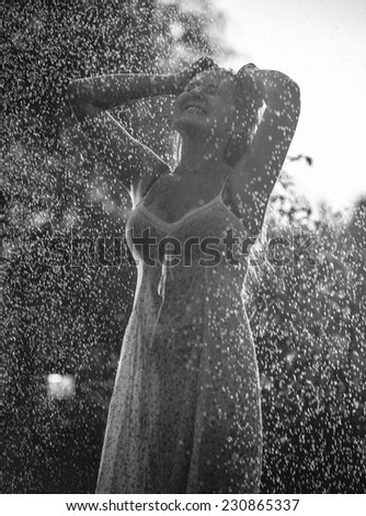 Black and white portrait of laughing woman enjoying water from garden sprinkle