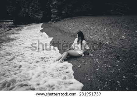 Black and white photo of young woman in white shirt lying on sea beach