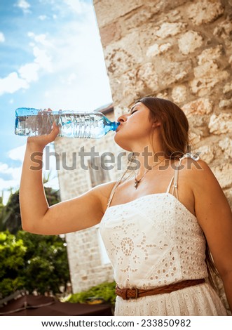 Closeup photo of young brunette woman drinking water out of bottle at sunny day