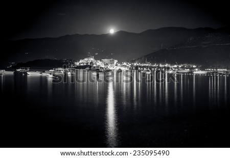 Black and white landscape of full moon shining over mountains, city and sea