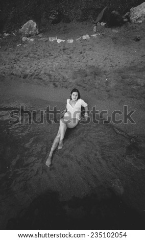 Black and white photo of sexy slim woman lying on sandy sea beach