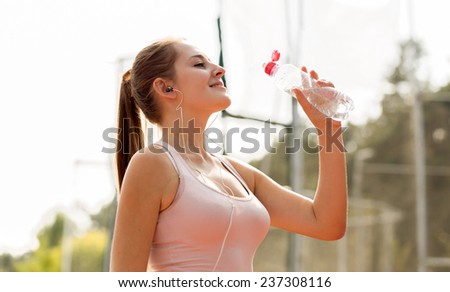 Beautiful smiling girl drinking water after running at hot day