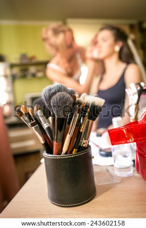 Closeup shot of set of professional makeup brushes against artist doing makeup to young woman