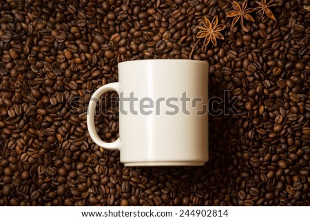 Closeup shot of white mug against coffee beans with anise stars lying like steam