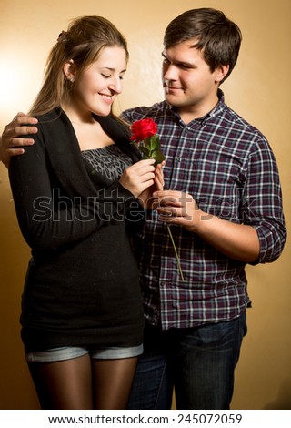 Studio portrait of smiling man giving red rose to cute girlfriend
