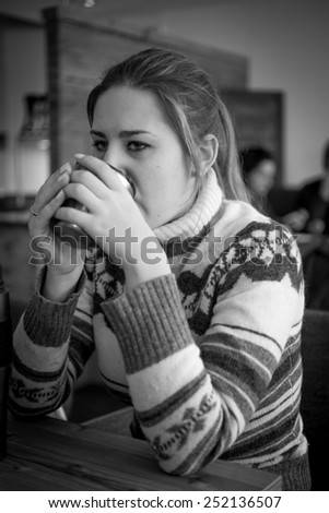 Black and white portrait of young woman in sweater drinking coffee at cafe