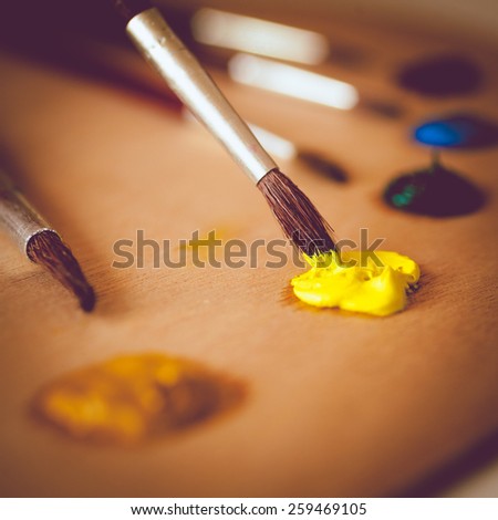 Closeup toned photo of paintbrush dipping in vivid yellow oil paint