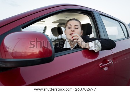 Beautiful woman looking in car side mirror and applying lipstick