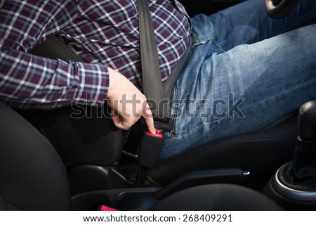 Young man driver pressing red safety belt button in car