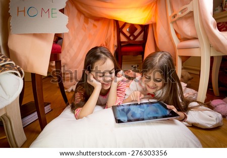 Two cute girls lying on floor at bedroom and playing on digital tablet