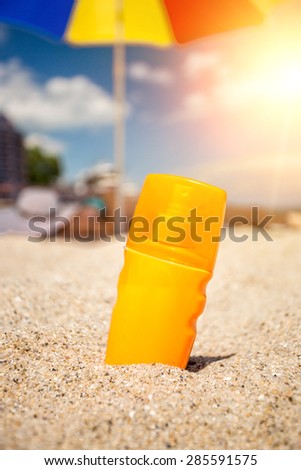 Closeup shot of yellow suntan lotion bottle lying on sand at beach