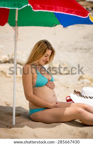 Young pregnant woman relaxing on beach and holding hands on stomach